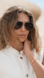 Women owned brand ANEA HILL model wearing silver aviators with sloped edge so you can wear with a hat