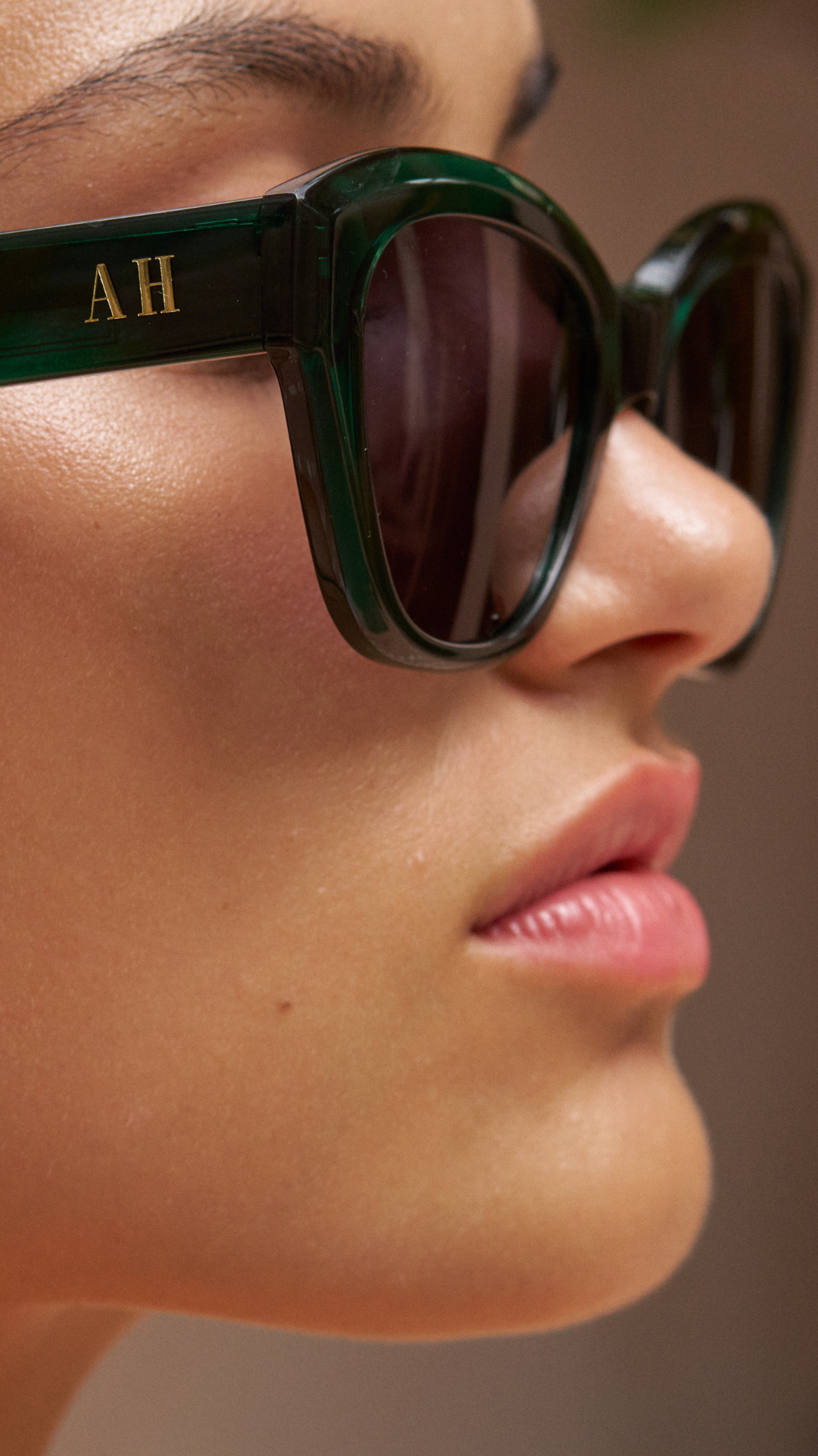 Clos up look of ANEA HILL green translucent luxury sunglasses for women fitting on a small face, smaller face with ANEA HILL AH logo on the side in gold.