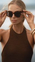 Load image into Gallery viewer, Our model wearing ANEA HILL&#39;s high-end Sunset Sunglasses, showcasing the oversized square frames and dark-tinted lenses for a chic and sophisticated look.
