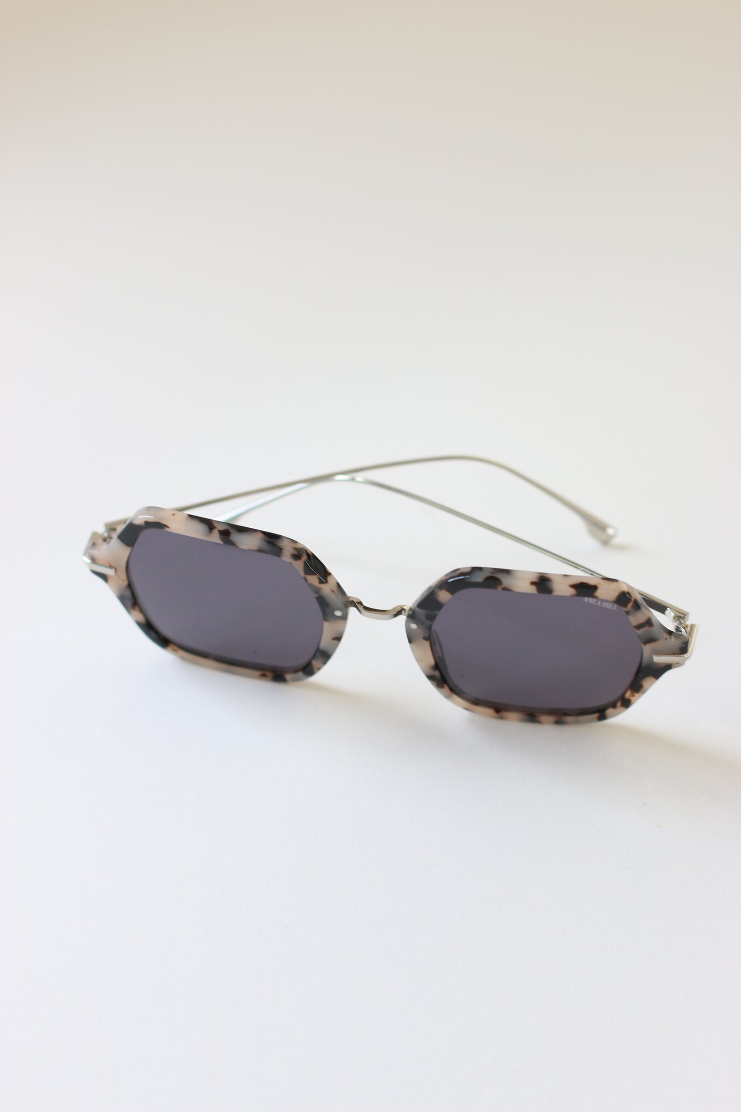 ANEA HILL's collection of luxury sunglasses features a top view of the First Class Sunglasses, revealing their elegant silver-tone accents and dark-gray tinted lenses.